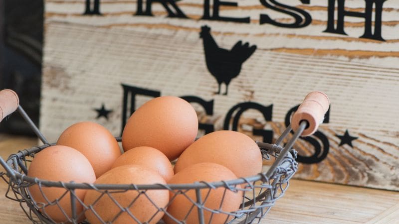 A wire basket filled with farm fresh eggs sits on a counter top.