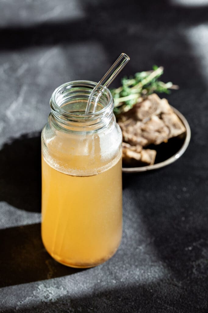 chicken bone broth in a glass with a straw for drinking. 