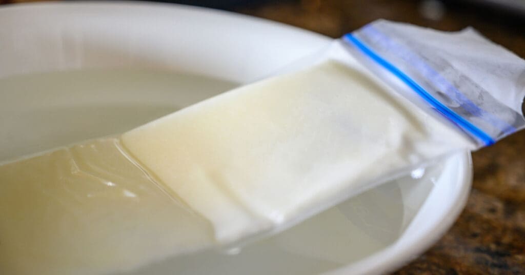 A plastic freezer bag of frozen raw milk thaws out in a bowl of cold water. If you freeze raw Jersey cow milk, this is the safest way to thaw it quickly. 