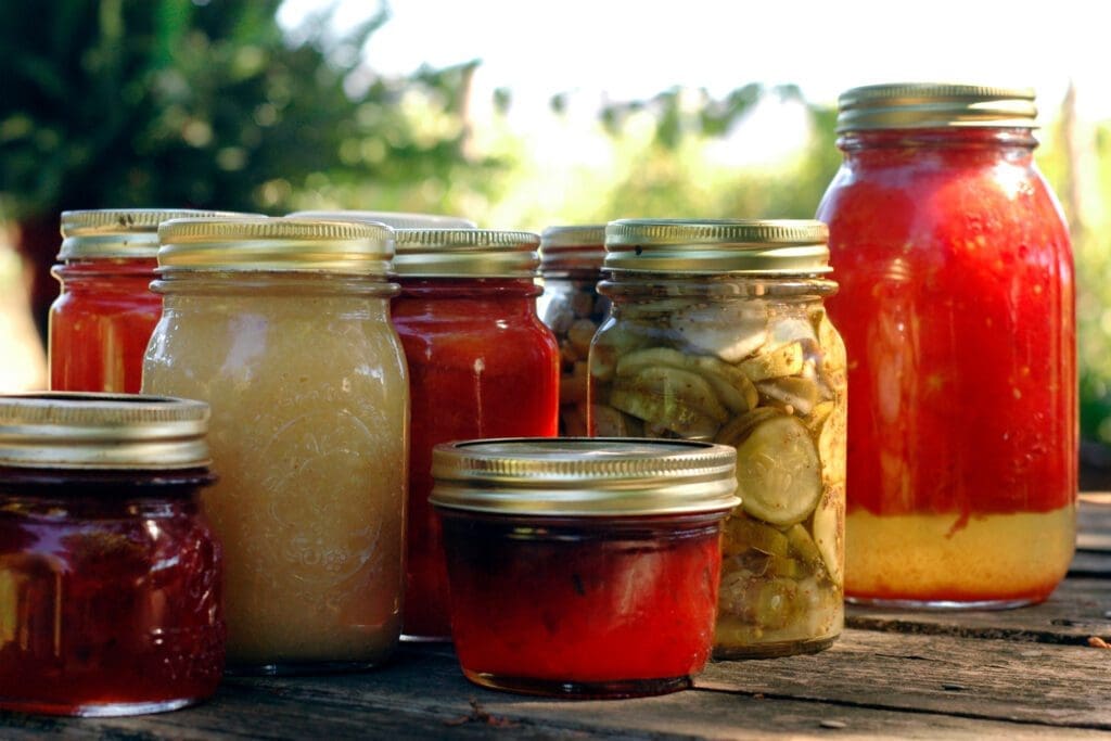 Several jars of preserved food sit on a table with canning lids tightly securing their contents. 
