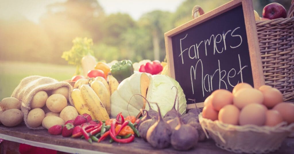 Farm-fresh eggs sit on a table next to other vegetables at a farmer's market. 