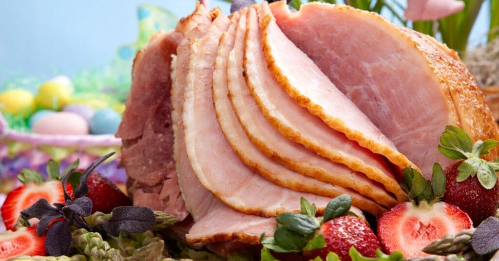 A ham sits on a dish of greens and fresh strawberries as part of an Easter feast meal. 